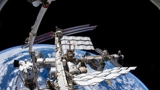 a fish eye lens view of the international space station with the canadarm extending up into black space. the earth is behind