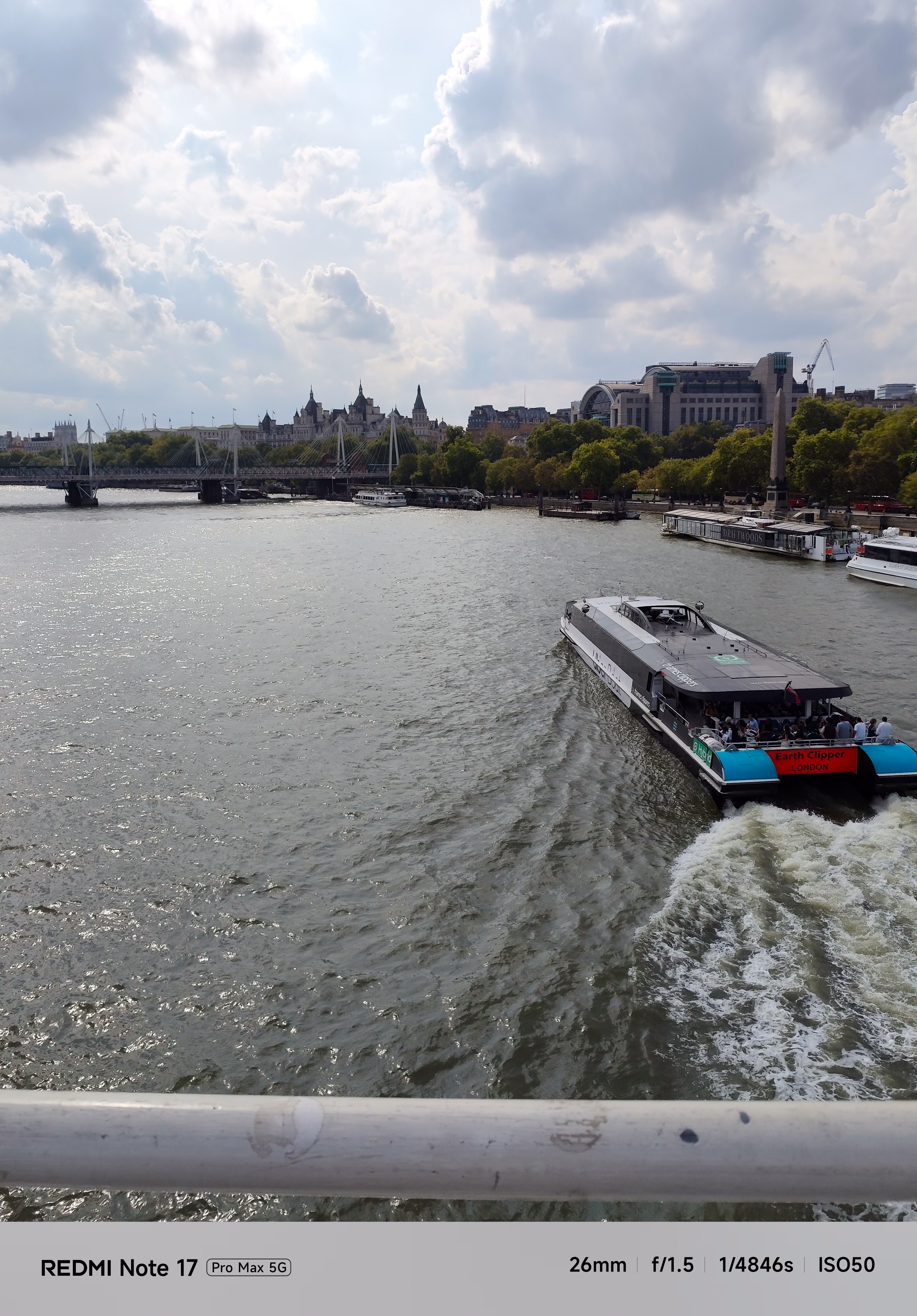 Boat traveling along the River Thames with bridges and central London buildings beneath dramatic clouds.