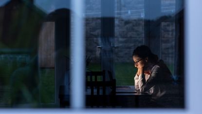 Woman sits inside as it is dark outside 