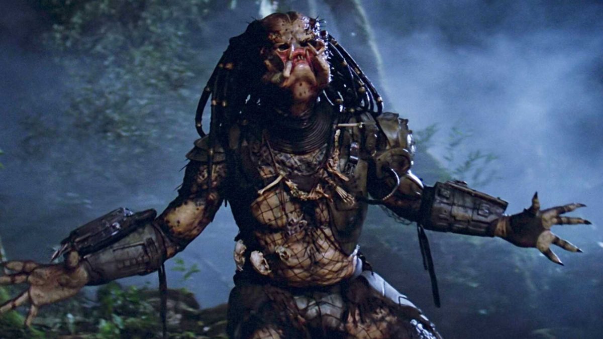 A still from the movie Predator of the Predator with its mask off and its arms spread out in the jungle, ready for battle.