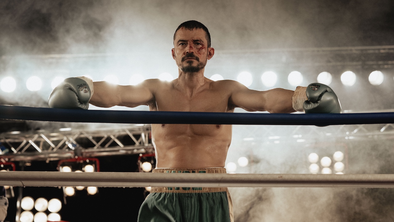 Orlando Bloom as “Boxer” in the Psychological Thriller film, with a bleeding face and his gloves against the ropes in THE CUT. 