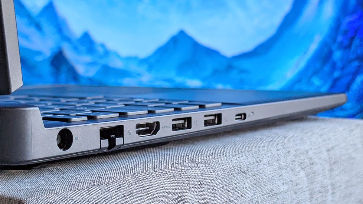 The left side of an Alienware 15 laptop shows multiple ports, including power, Ethernet, HDMI, two USB‑A ports, and a USB‑C port, with a blue-toned landscape wallpaper visible on the screen.