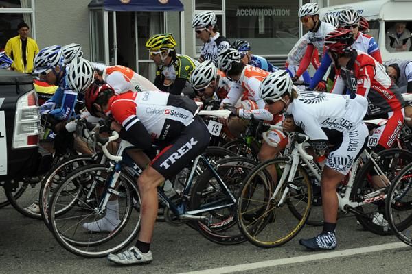 Riders shelter from the cold wind behind the race directors vehicle before the start of stage five