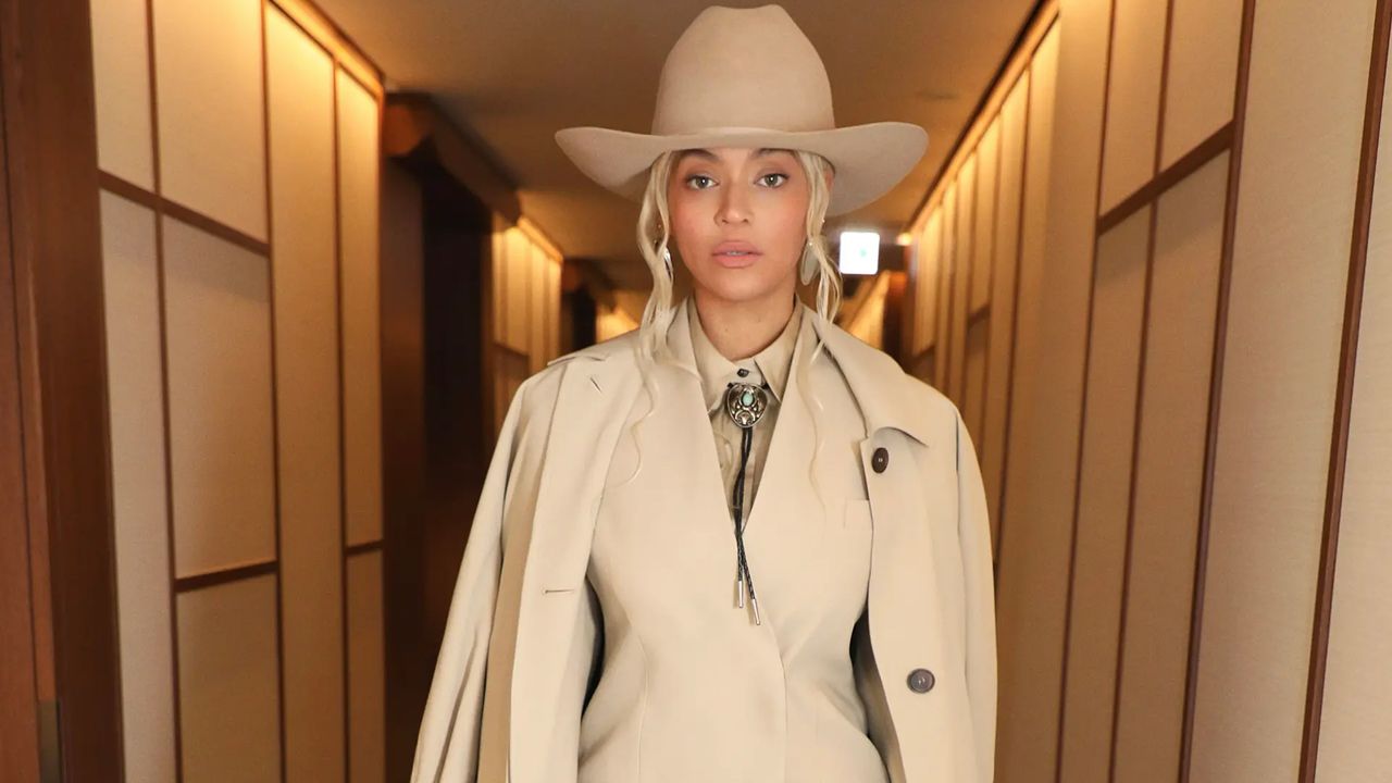 Beyonce wears a tan Ferragamo suit with $36 earrings in front of a plain wall