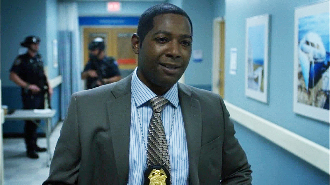 Brett Mahoney wearing a suit and his NYPD badge around his neck in Netflix's Daredevil TV show