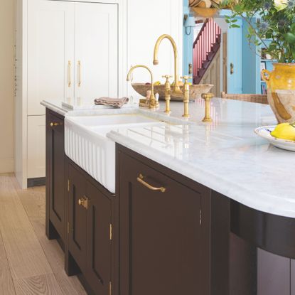 Kitchen island with black cabinets, a white marble countertop and gold taps