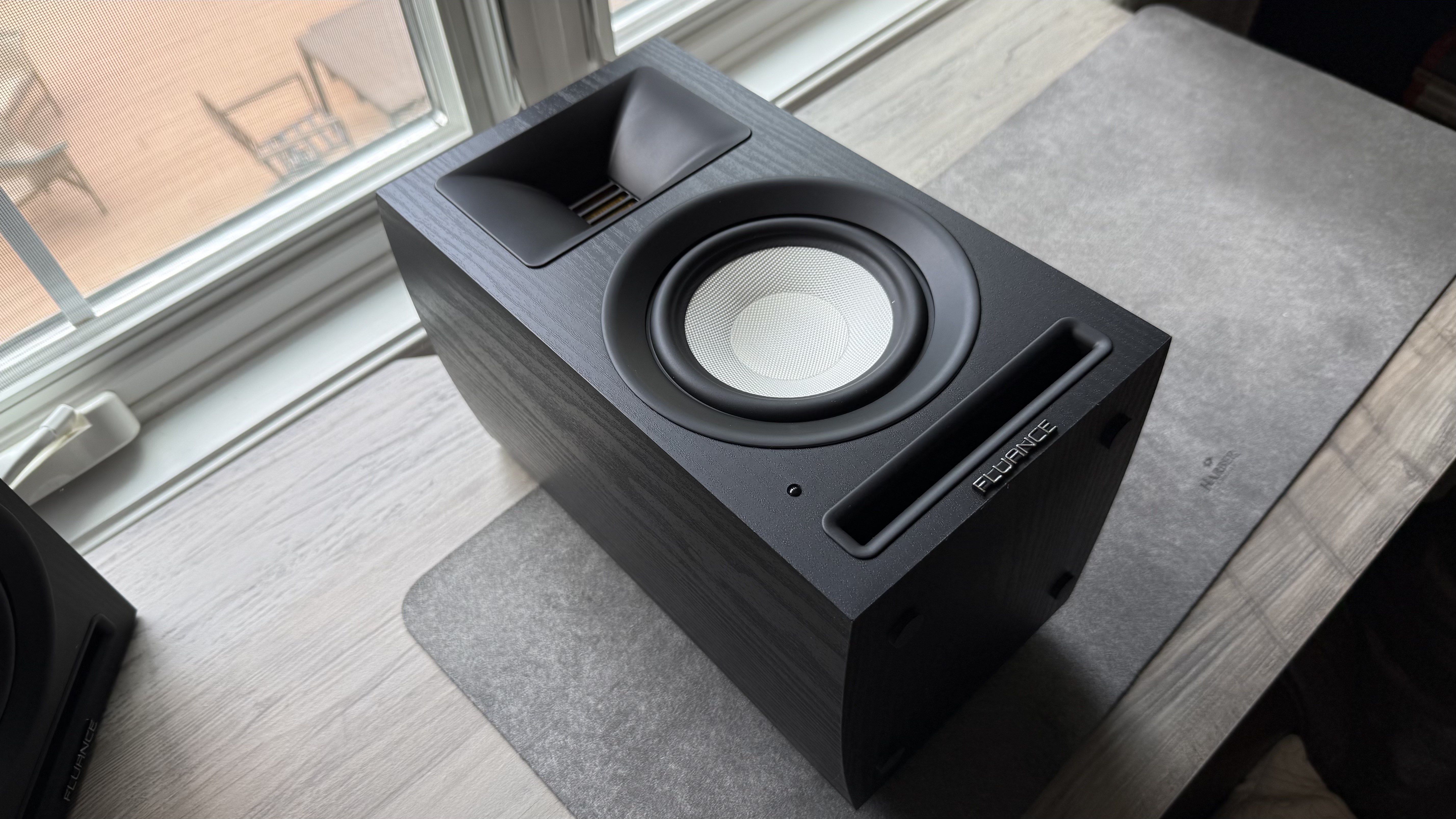 Black Fluance Ri71 powered bookshelf speaker facing up and placed on its back on a windowsill.