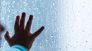 Childs hand on window pane with condensation on the outside