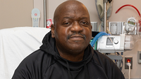 Close-up picture of Rick Slayman. He is sat on a hospital bed and wearing what looks like a black sweatshirt. 