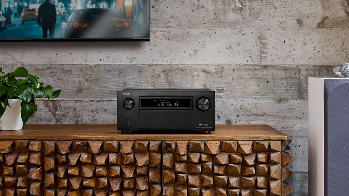 Denon AVC-A10H sitting on a jagged wood unit with a plant on the left hand side and speaker to the right