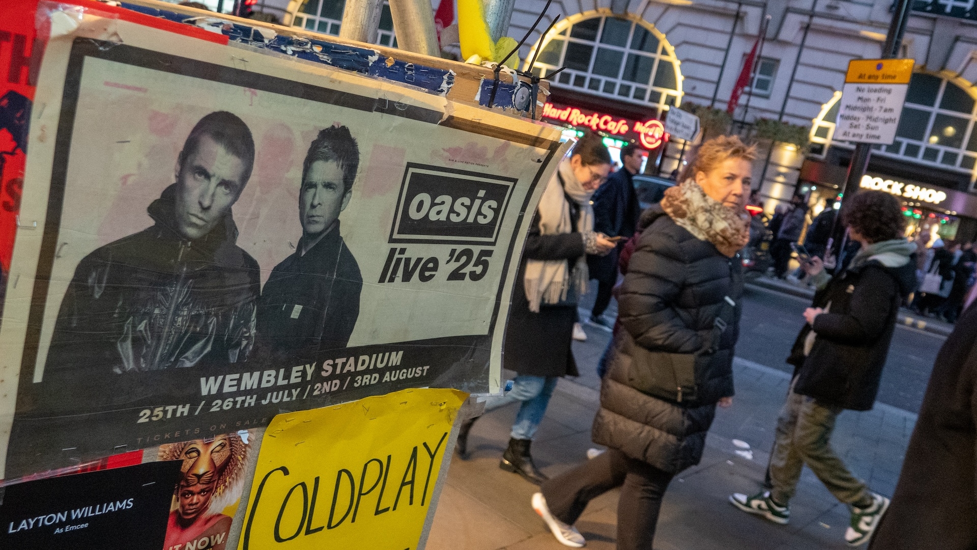 People walking past the Oasis 2025 tour poster in London