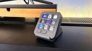 The Logitech MX Creative Console keypad and stand on a black desk in front of a wood monitor stand