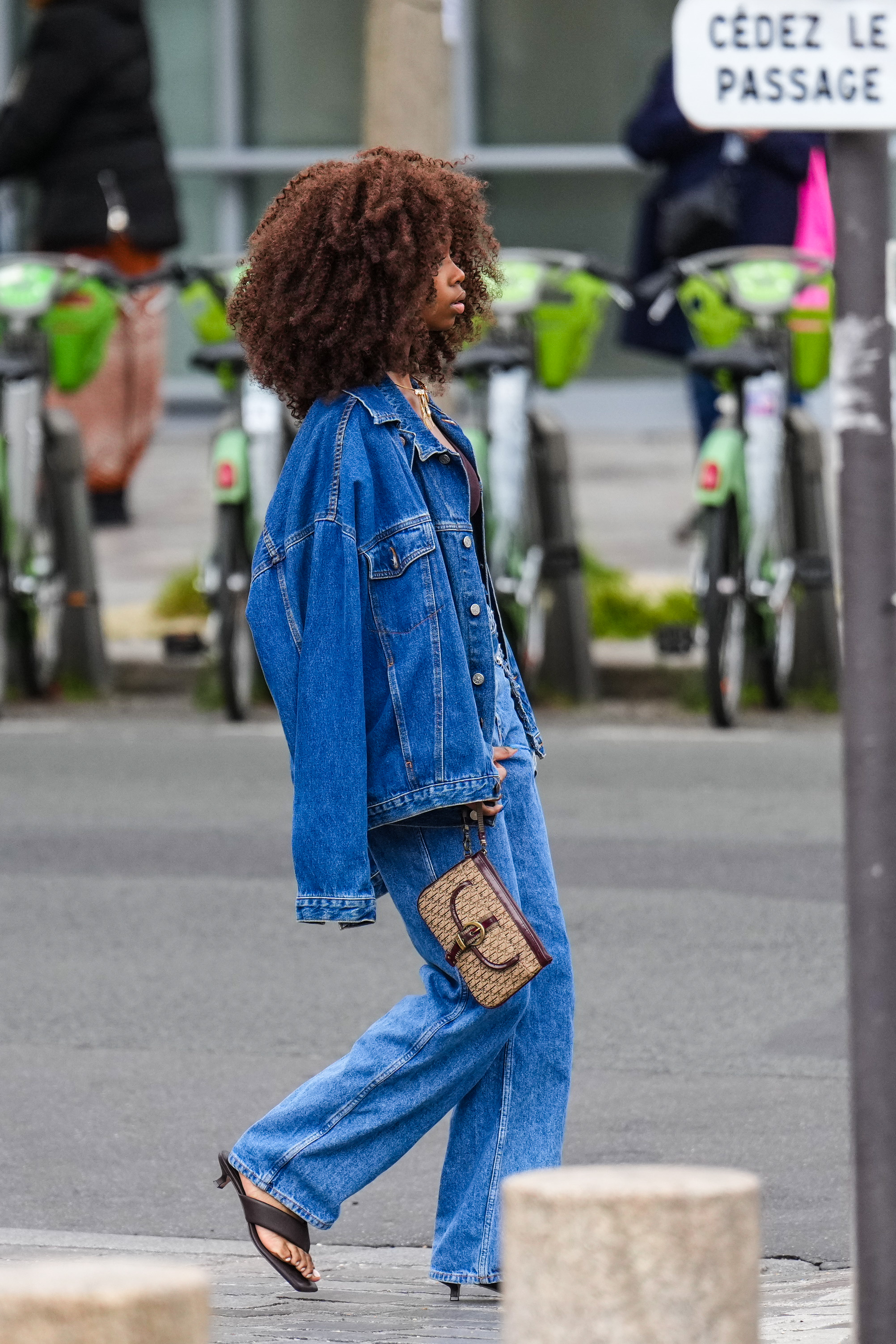 A guest wears a navy blue denim oversized jacket, blue denim jean pants, dark brown shiny leather heels flip flop / mules in Paris, France.