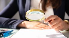 A businesswoman uses a magnifying glass to look at financial paperwork.