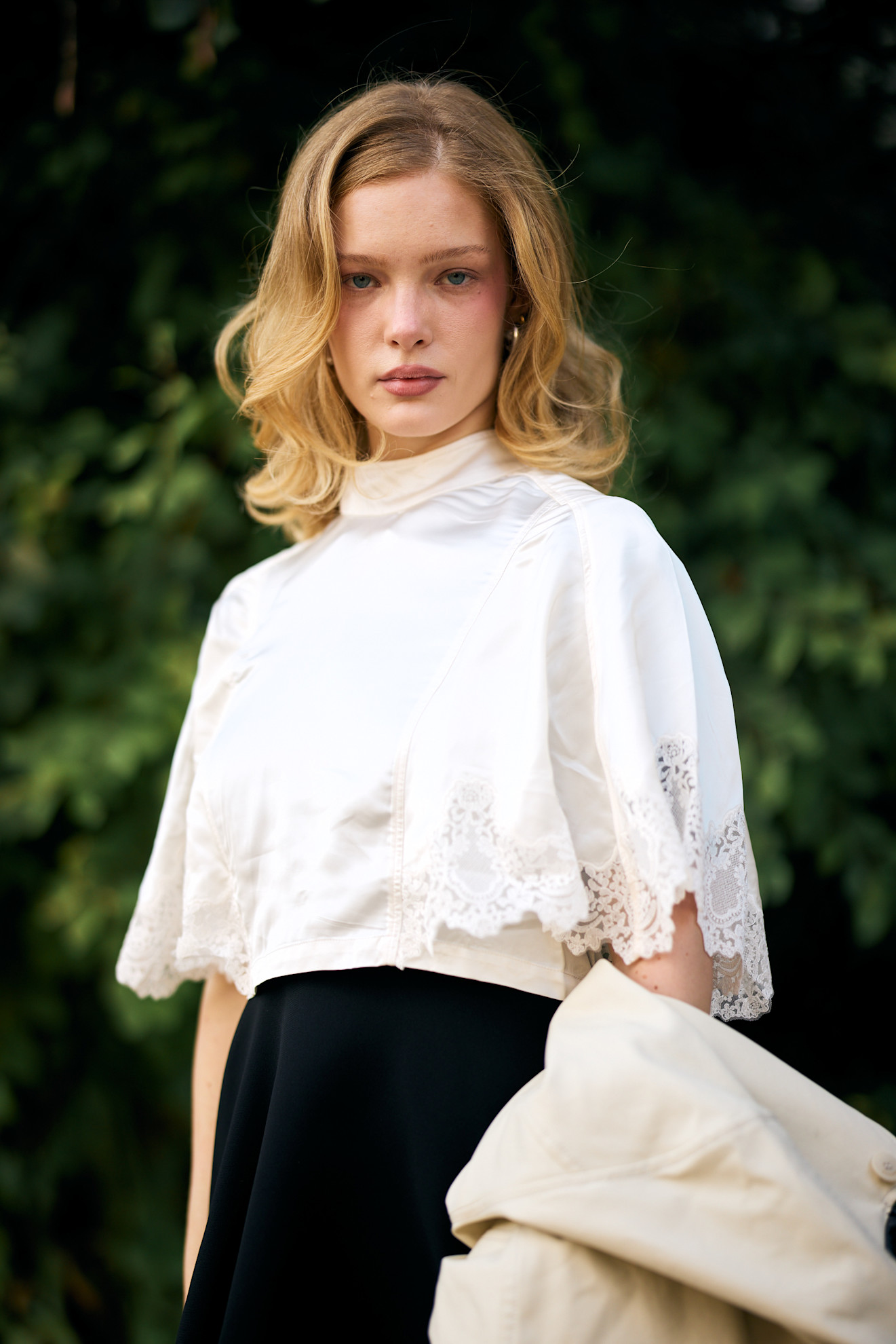 a white woman with a blonde blowout in a white top and black skirt