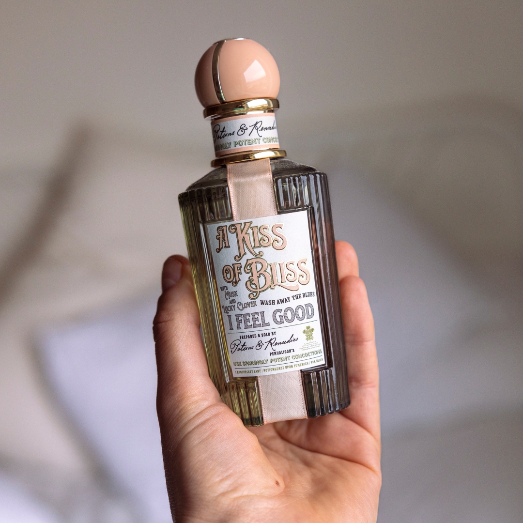 A close-up of Audience Development Manager, Lauren Scott's hand seen holding a bottle of Penhaligon's Kiss Of Bliss perfume, in front of a cream and white background