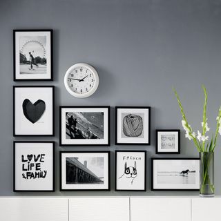 Mid grey wall with L-shaped gallery wall of art in black frames with a white sideboard beneath