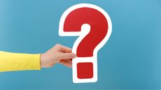 A woman's hand holds a red question mark outlined in white against a blue background.