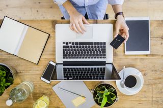 Financial wellness: Top view of woman at wooden desk with credit card and laptop
