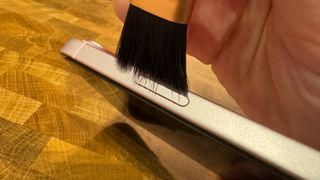 Cleaning the stuck iPhone 15 Plus lock button with a brush