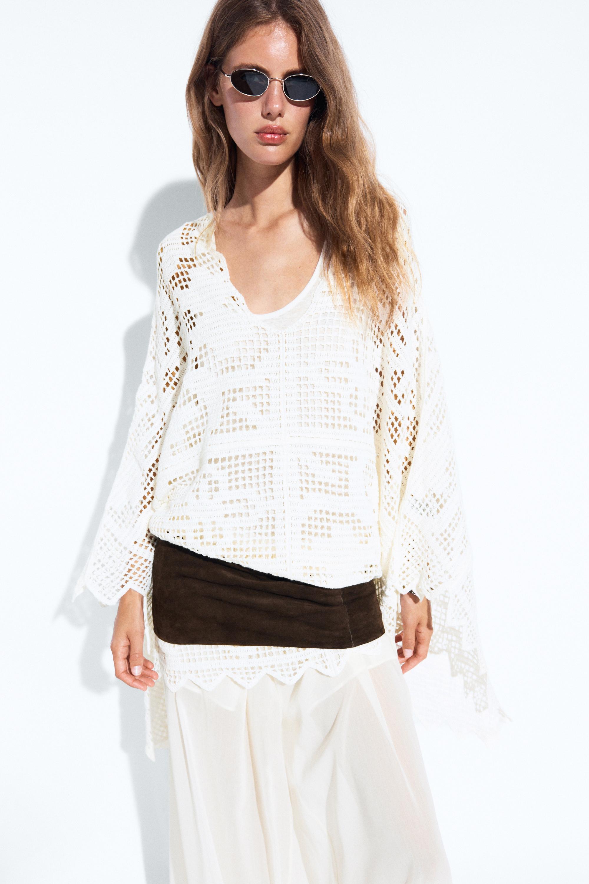 An image of a model wearing a crochet cape with a brown belt