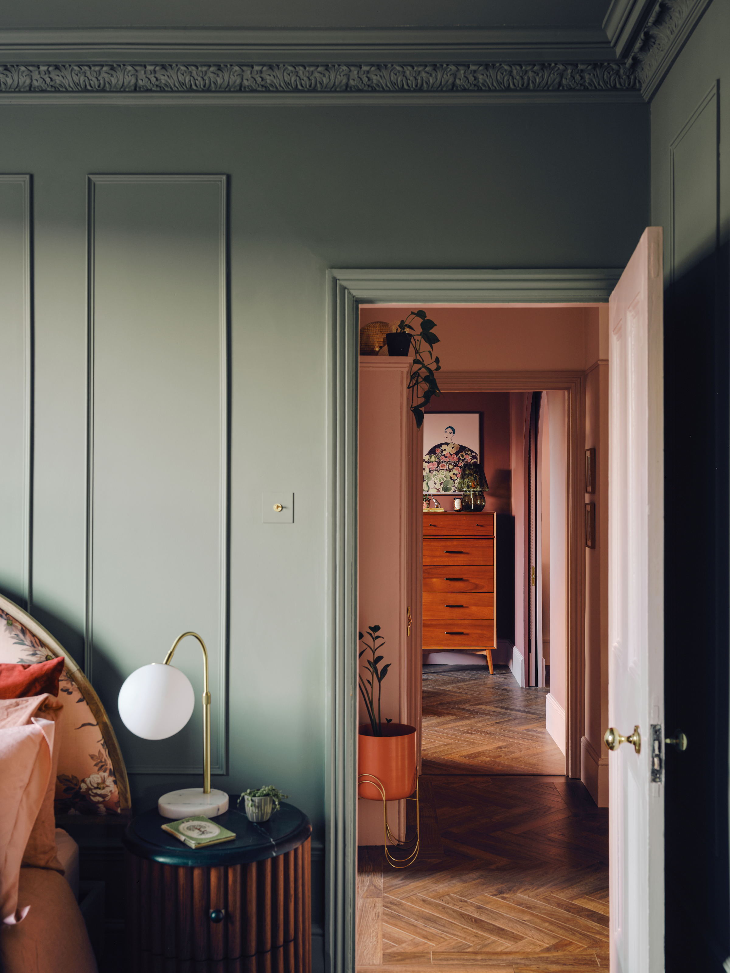 Green bedroom with panelled walls, arched floral pattern headboard and fluted round side table