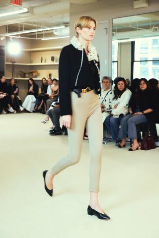 Altuzarra model wearing a cropped black jacket and tan cigarette pants with black flats.