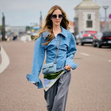 Woman wears denim jacket, gray trousers, scarf, and heels. 