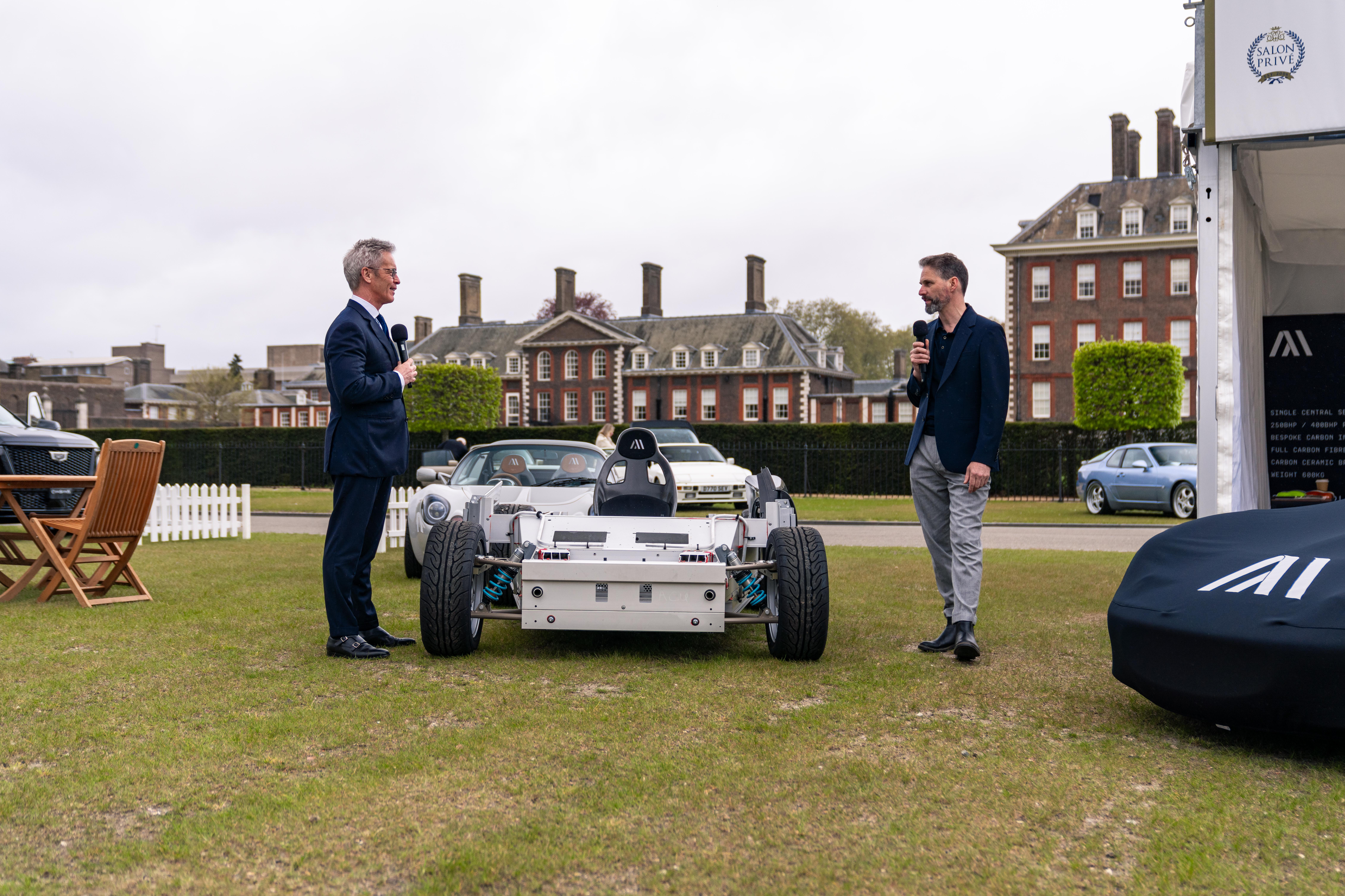 Two men chat over a shell of a car