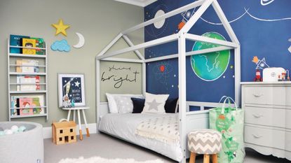 Child&#039;s bedroom with four poster bed, mural of planets, grey carpet, chest of drawers and bedding. 