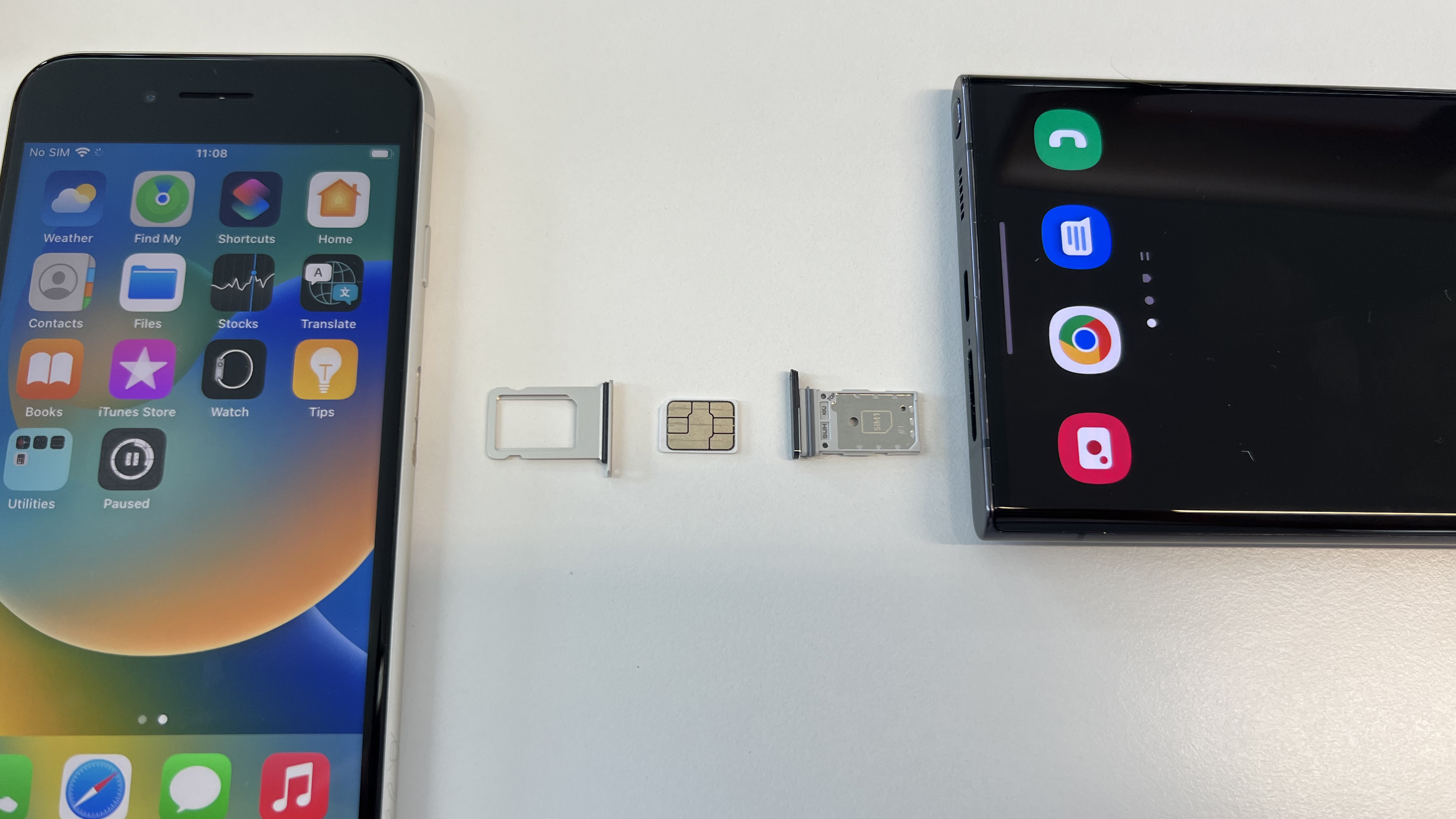 An iPhone SE 2022 and a Samsung Galaxy S22 Ultra with their SIM trays removed and a nano SIM card positioned between them