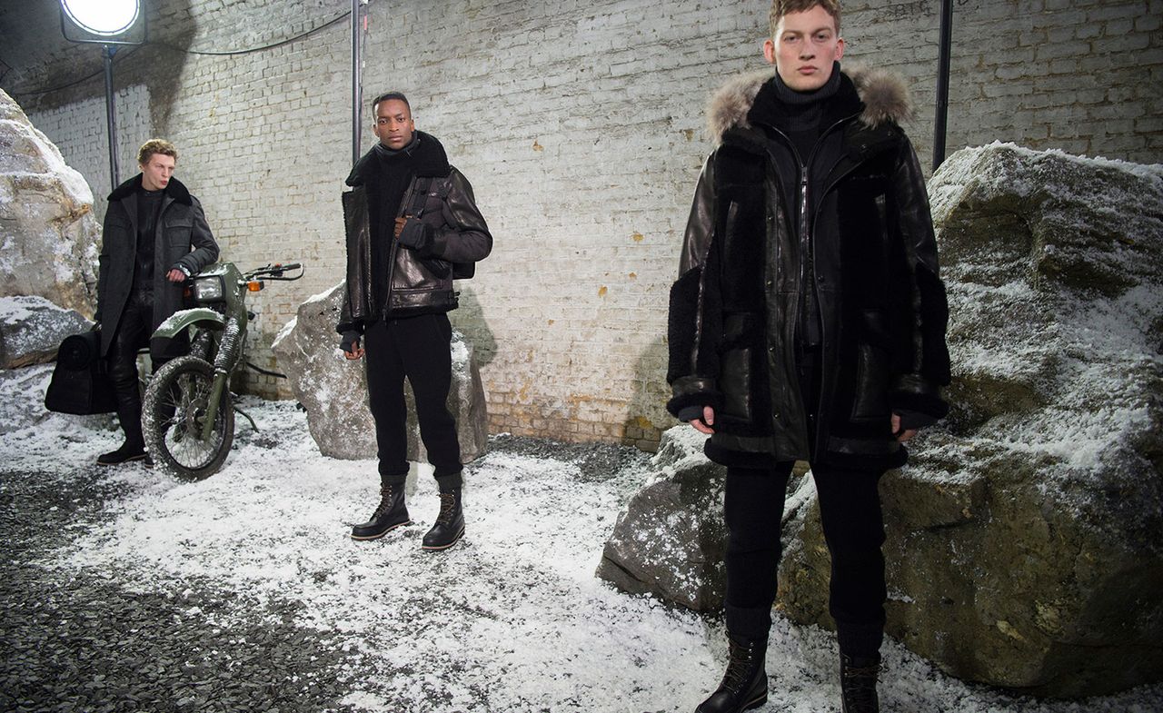 Three male models stood in the snow with black coats on