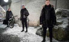 Three male models stood in the snow with black coats on