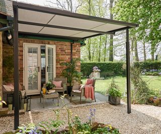 Thomas Sanderson's premium pergola awnings attached to the side of a red brick house with rattan garden furniture