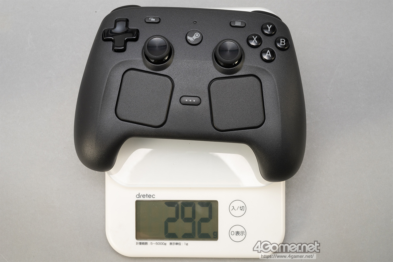 A black gaming controller is placed on a digital scale displaying 292 grams. The setup is on a light gray surface, conveying a neutral tone.