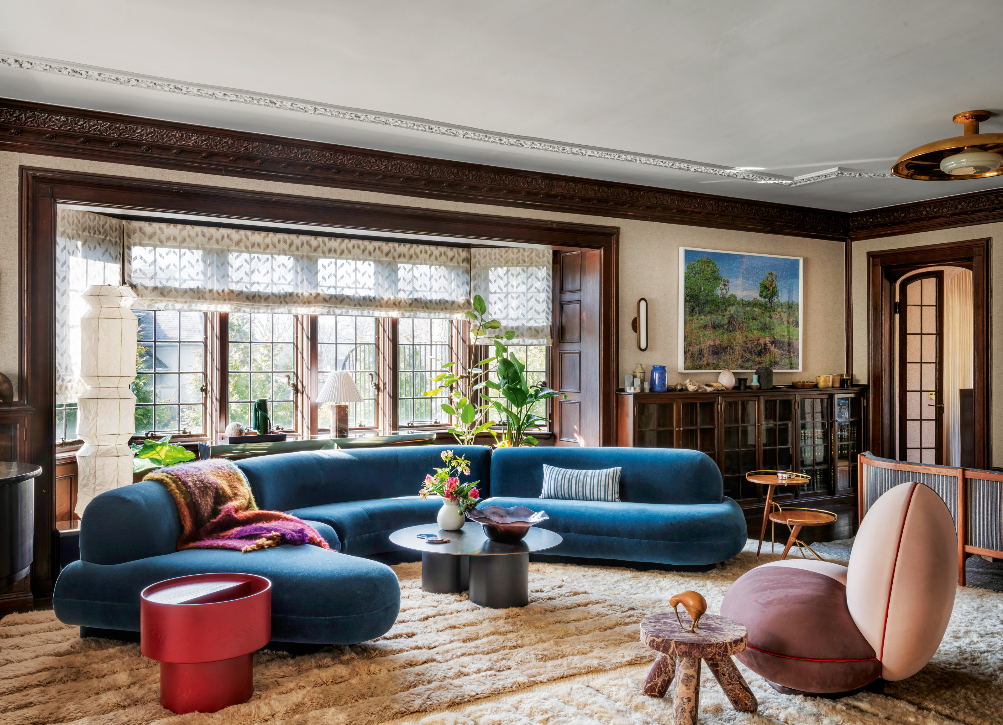 Living room with original beams and period details, contemporary blue curved sofa, red side table, pink accent chair and deep-pile rug