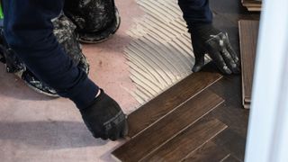 Man laying dark wood herringbone flooring with glue