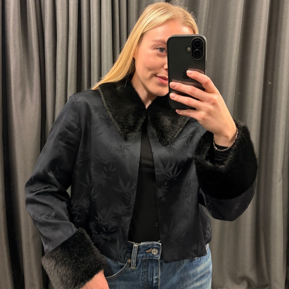 Florrie wears a black jacket with faux fur collar and cuffs, black top and blue jeans 