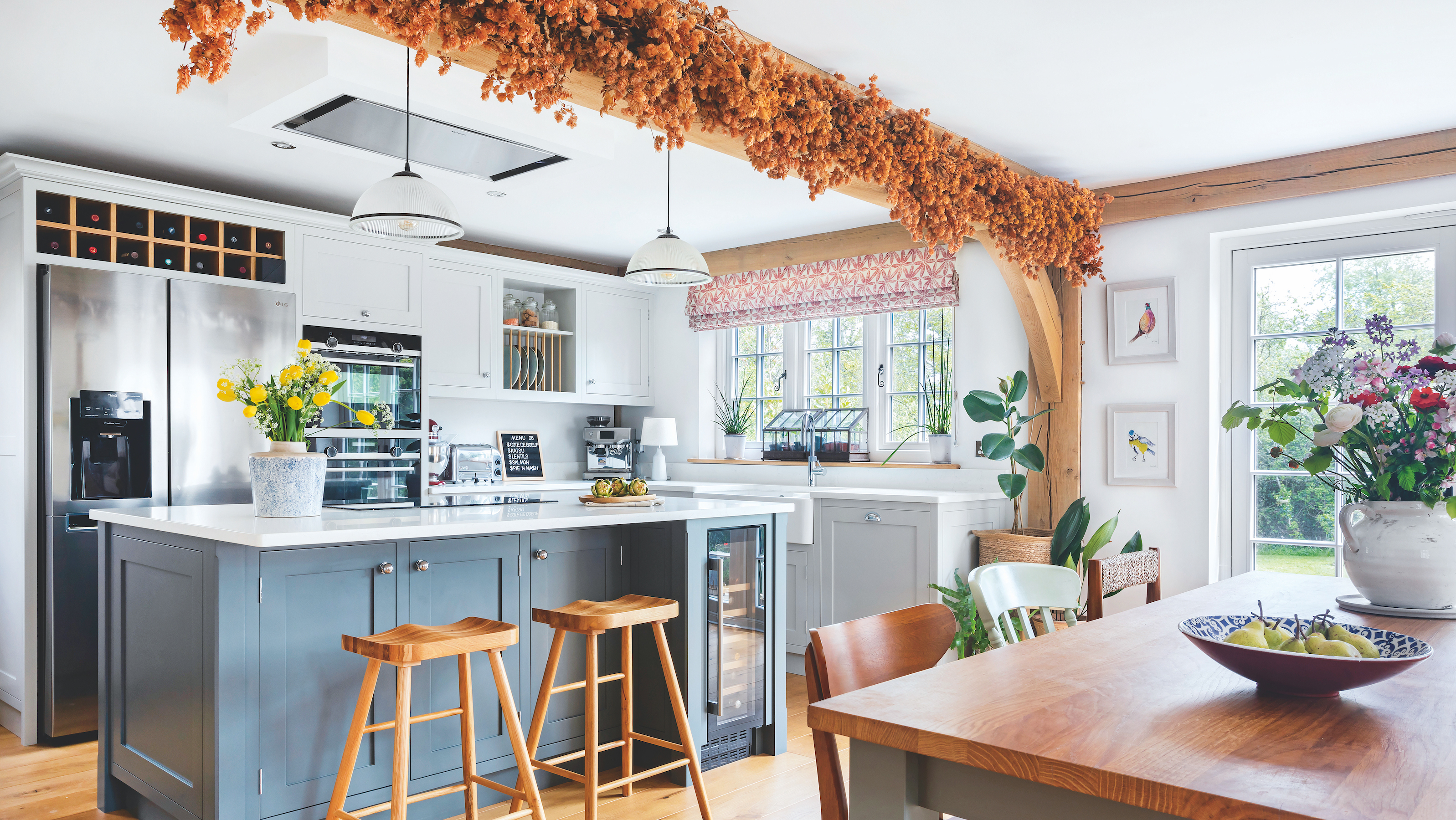 kitchen in oak frame house with blue island, large stainless steel fridge and dried hops on ceiling beam