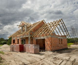 A red brick house in construction with a pitched timber roof with no roof tiles