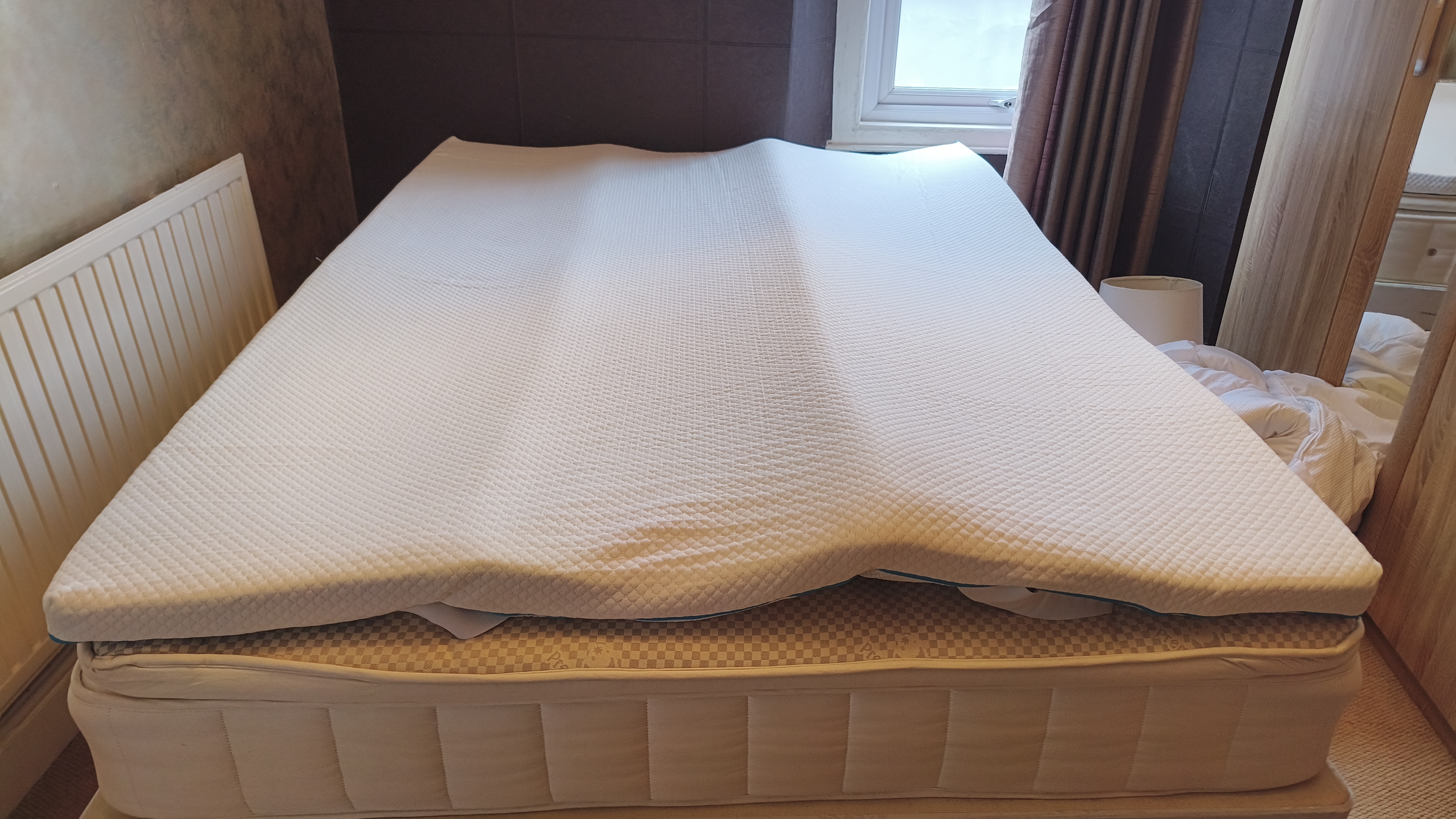 The Simba Cool Foam Mattress Topper laid flat and unstrapped on a double bed, showing its full coverage of the mattress surface.