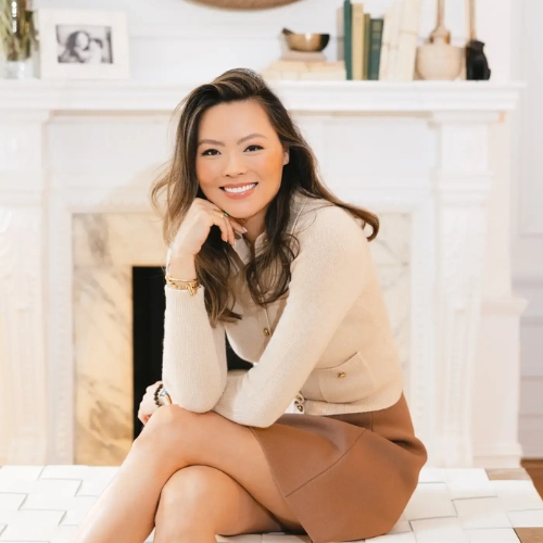 Image of a woman in a beige sweater and tan skirt sitting on a white bench.