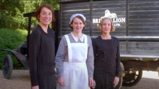 Raquel Cassidy, Sophie McShera, and Joanne Froggatt standing outside smiling in front of a supply truck in Downton Abbey: A New Era.