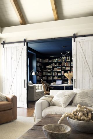 A living room with sliding barn doors leading into a cobalt blue study space beyond