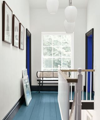 hallway with white walls, large window, mid-blue wooden flooring, trim work painted black and bright blue