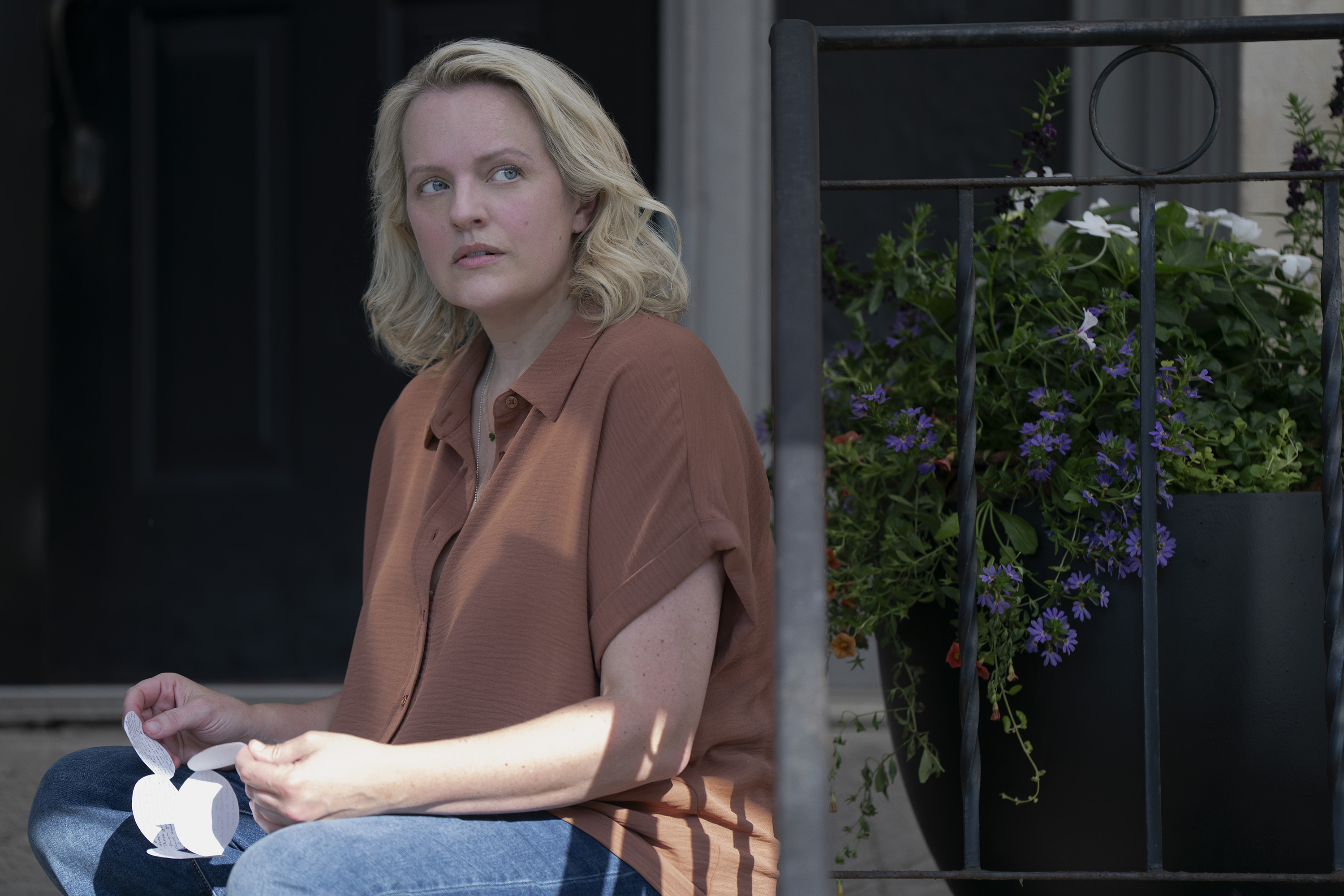 Elisabeth Moss' character June Osborne sits on a porch in a scene from 'The Testaments.'