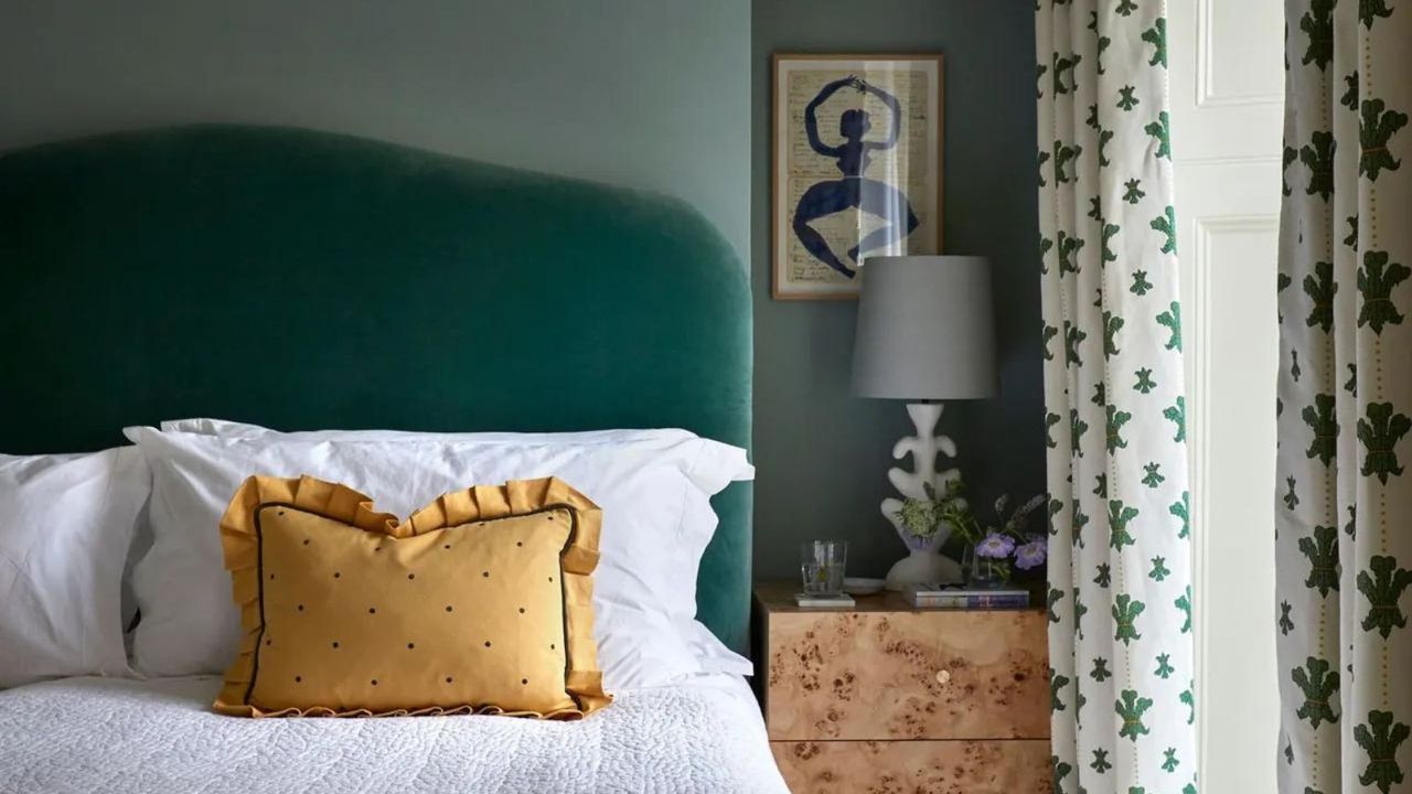 A bed with a green velvet headboard and a yellow scatter pillow