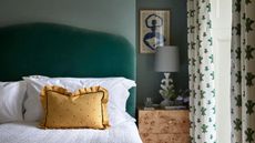 A bed with a green velvet headboard and a yellow scatter pillow