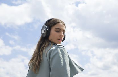 A woman wearing the Focal Bathys headphones, infront of a cloudy sky.