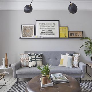 living room with white wall and picture frame and grey sofa with cushions and white side table